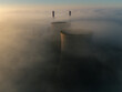 © AmazingAerialAgency - Aerial view of the RWE Clauscentrale power plant cooling towers and chimneys emerging from a thick layer of morning fog in Maasbracht, Limburg, Netherlands.