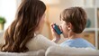 © olga_demina - A woman assists a young boy in using an inhaler in a warm and inviting living room. The scene conveys care, support, and a sense of normalcy in managing health.