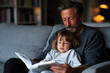© Milos - Father and Child Snuggled on Couch Reading Book, Warm Family Bonding and Shared Storytelling, Cozy Learning Moment, Soft Natural Light, Authentic Lifestyle Scene