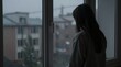 © Cloudyew - Lone woman stands by a rain-streaked window