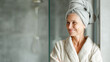 © Kowit - A mature woman in a bathrobe with a towel wrapped on her head smiles in a modern bathroom.