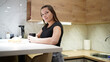 © Vasyl - Young woman sitting in kitchen holding hot drink and looking at camera in bright modern interior