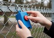 © Mozida - Hands holding blue device with red button near chain link fence