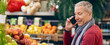 © Prostock-studio - A person is talking on a mobile phone while standing near a display of fruits at a grocery store. The store has many colorful fruits on display.