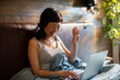 © Davor - Smiling woman waving on video call in bed at home