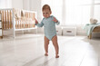 © New Africa - First steps. Cute little baby in onesie with toy xylophone learning to walk at home
