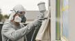 © Bakha - Painter using spray gun applying paint on house exterior wall with protective gear