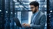 © Gophotograph - Male admin working on a laptop while focusing on cybersecurity in a server room.