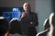 © Seventyfour - Senior Caucasian businessman presenting AI strategy during conference, speaking to audience beside digital screen. Ideal for business innovation, leadership training, tech events