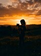 © hamad - Silhouette of a young man and a girl with a camera at sunset showing a romantic family moment outdoors