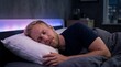 © D-point - Caucasian man sleeping peacefully in bed at night. Relaxed male resting on pillow in bedroom with glowing led illumination. Healthy lifestyle, recovery, comfort and deep sleep concept.