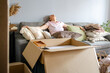 © Ina - Tired middle aged woman resting on sofa among cardboard boxes and packed belongings after relocation. Moving exhaustion, overwhelming unpacking, burnout and difficult lifestyle transition concept.