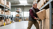 © OlgaNeuroArt - Mature male warehouse worker lifting a heavy cardboard box. Senior man in work gloves stacking packages on a shelf in a large industrial storage facility. Logistics and inventory management