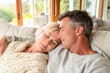 © Kowit - A mature couple relaxes on a cozy sofa at home, leaning on each other with peaceful, content expressions, enjoying a quiet and intimate moment together.