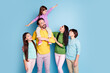 © deagreez - Happy family portrait with parents and three children laughing together, playful father carrying daughter on shoulders against a bright blue background
