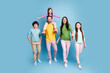 © deagreez - Happy family portrait of parents and three children walking together against a studio blue background, smiling and holding hands in bright casual clothes