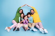 © deagreez - Happy family of five sitting together forming a roof with their arms on a blue background — parents and three children smiling in a casual, colorful studio portrait showing love and togetherness