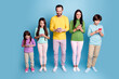 © deagreez - Family using smartphones together standing in studio on blue background with parents and children engaged in mobile technology and digital connectivity