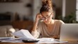 © Aditya - Woman feeling stressed while reviewing financial documents and tax forms at her home office.