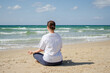 © Юлия Завалишина - Yoga calm mindfulness meditation. Young healthy woman practicing yoga on beach. Woman sitting in lotus pose meditating relaxing connection with nature by the sea. Girl doing breathing practice