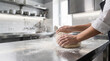 © Helena GARCIA - Manos de cocinera profesional amasando pan en una mesa de acero inoxidable de una cocina de restaurante luminosa