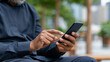 © pattozher - Texting in Urban Oasis: Close-up shot of hands texting on a modern smartphone, set against a blurred urban background, creating a juxtaposition of technology and the outdoor environment.