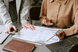 © AnnaStills - Close up of businesswomen reviewing analytics report, pointing at charts, discussing strategy during meeting. Ideal for teamwork, financial planning, consulting, corporate communication