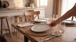© Laura - Close up of a person setting a modern dining table with plates and glasses for a family meal.