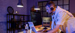 © Pixel-Shot - Young bearded programmer with headphones working in office at night