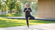 © TheLestari - Senior Asian woman practicing yoga tree pose outdoors