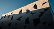 © GraphicX - A modern building with a unique geometric facade design, featuring a pattern of triangular and polygonal shapes in varying shades of gray and white, with windows of different sizes and shapes.