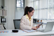 © MINAE - Businesswoman working in modern office, analyzing financial data on documents, using laptop and smartphone, managing multitasking tasks, planning strategy and increasing productivity