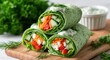 © binara - Green spinach tortilla rolls filled with crunchy vegetables and creamy sauce on a wooden platter for vegetarian restaurant advertising