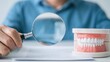 © 69 - Close-up of person examining artificial teeth model with magnifying glass on white surface for dental study or health inspection concept