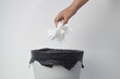 © Maule - Hand throwing crumpled white tissue paper into a trash bin with a black plastic liner against a white background.