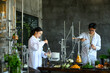 © Prathankarnpap - Two Asian Scientists in Lab Coats Conducting Herbal Extraction Research with Glass Distillation Equipment and Fresh Botanicals
