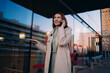 © BullRun - Middle aged business woman using mobile phone for international call, standing outdoors, urban glass architecture, evening light, wireless communication, technology, holding gadget, talking.