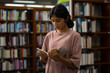 © NVB Stocker - Young Indian teenage girl smiles and selects blue book. Her fingers gently touch the cover's edge. Behind her, wooden shelves hold many books. Education, Back to school
