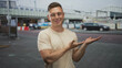 © Krakenimages.com - Man with glasses gesturing open palm while smiling and presenting toward camera at a train station in beige t-shirt, visible hands and forearm; friendly welcome.