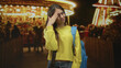 © Krakenimages.com - Teenage girl with blue backpack touching her temple and wincing before a lit carousel at an amusement park, showing headache; discomfort.