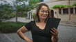 © Krakenimages.com - Woman holding tablet and smiling with hand on hip, looking at screen in a sunlit stone building courtyard; happiness connection.