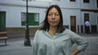© Krakenimages.com - Woman standing with hand on hip wearing pale blue shirt on city street near lamp post and green window shutters; pensive reflection.