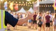© SimpleDesignStudio - Security guard in high visibility vest directing crowd at outdoor music festival event with blurred audience in background