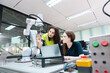 © eakgrungenerd - Engaged young woman student engineer in teamwork, learning about robot technology with robotic arm. Future education for industry automation and modern programming for machinery