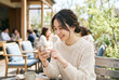 © ye - 屋外カフェでスマートフォンを操作する人物、日常生活とテクノロジー利用の風景