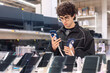 © Светлана Мищенко - Teenage boy choosing smartphone in electronics store. Technology shopping, consumer decision making, mobile device comparison and digital lifestyle concept.