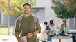 © DMegias - African American student smiling, holding a notebook, wearing a backpack, with classmates relaxing in the background. Studying outdoors