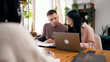 © DMegias - Couple reviewing documents and using a laptop while meeting with a financial advisor at a wooden table in their home
