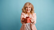 © DMegias - Mature woman smiling, presenting a beautifully wrapped red gift box forward. Studio shot with a turquoise background