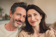 © Kowit - A happy middle-aged couple smiles warmly, sitting closely together in a cozy, softly lit home environment.